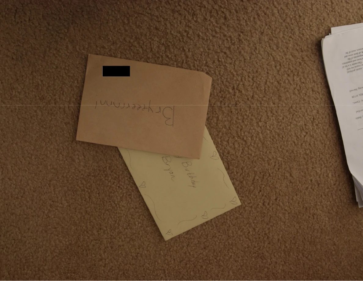 Brown envelope with a small black redaction over part of its face, resting on a yellow greeting card.