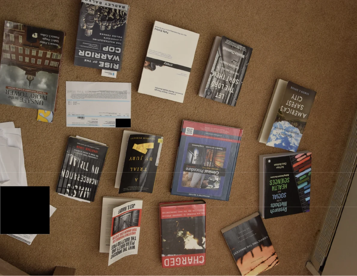 Books and papers arranged on carpet, with black redactions covering parts of two papers.