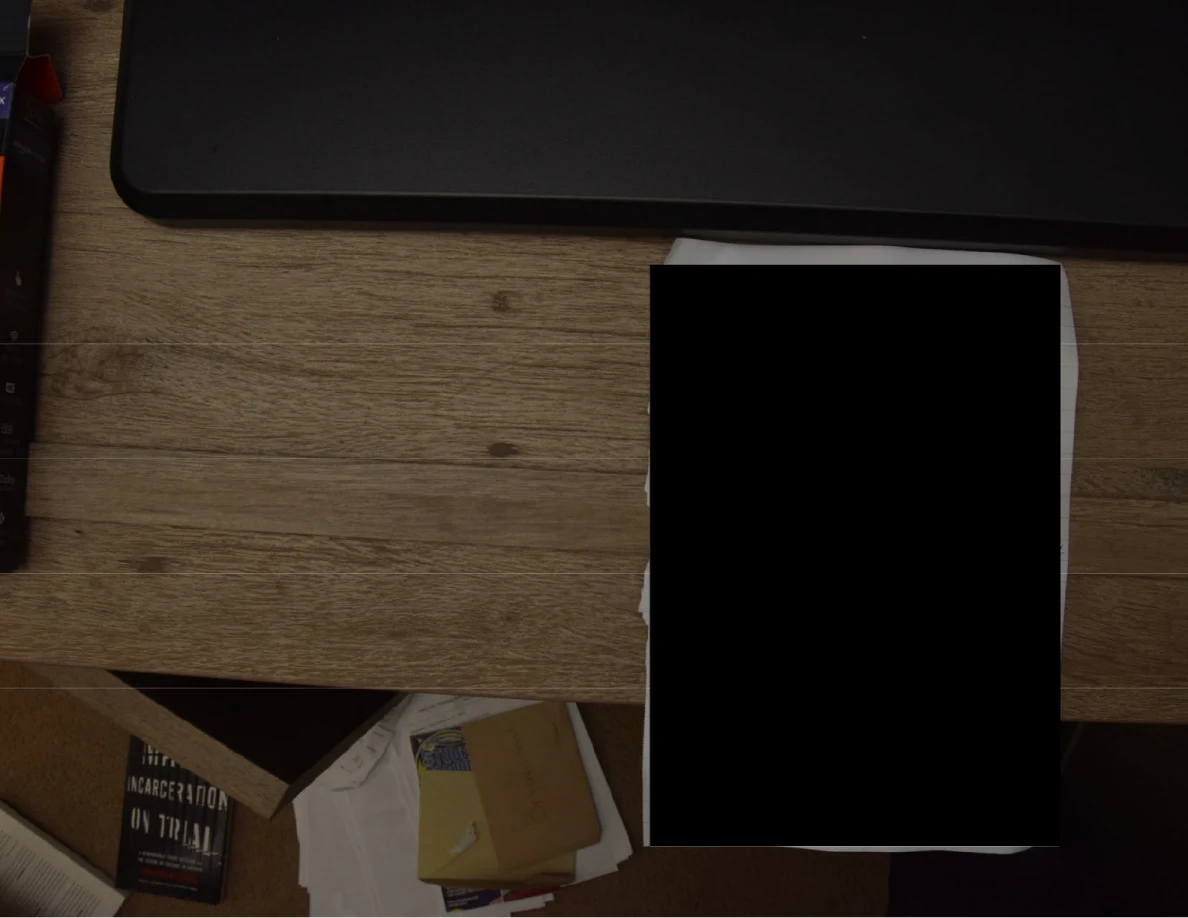 Paper on a wooden surface almost entirely covered by a black redaction.