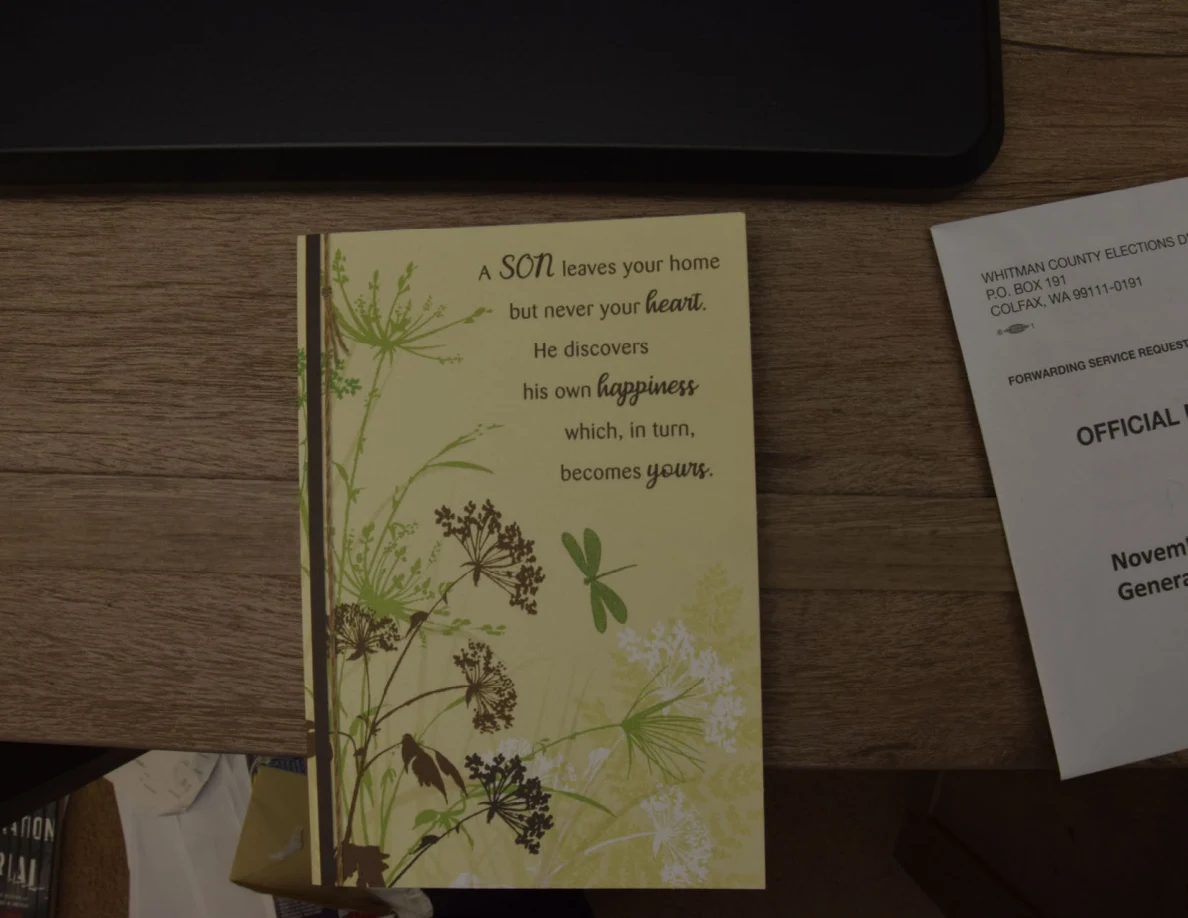 Floral greeting card about a son leaving home, lying on a wooden surface.