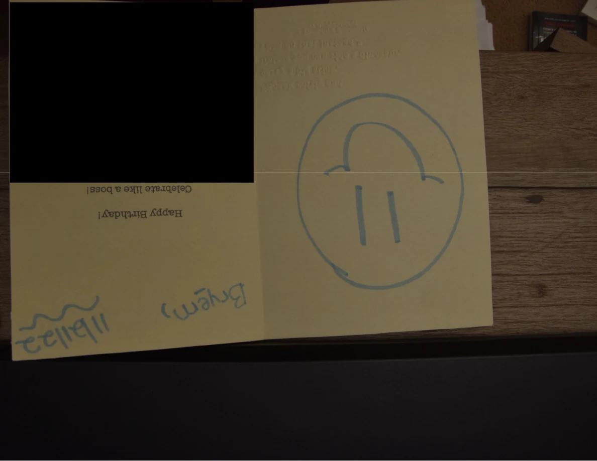 Open yellow birthday card with a large blue smiley face and a black redaction.