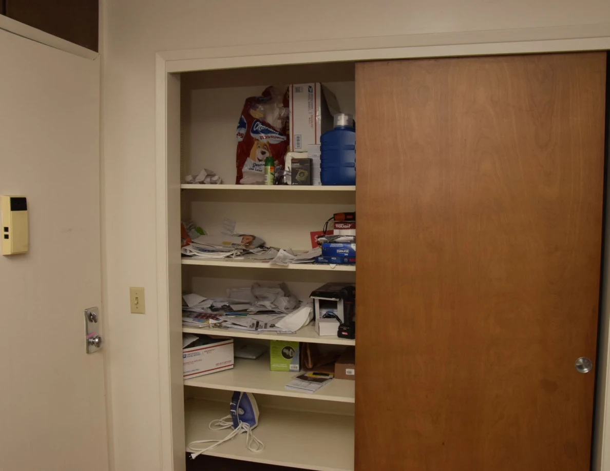 Upper view of a cluttered storage closet behind a sliding wooden door.
