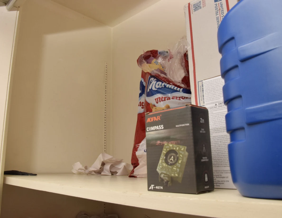 Closet shelf with a compass box, paper-product package and large blue plastic container.