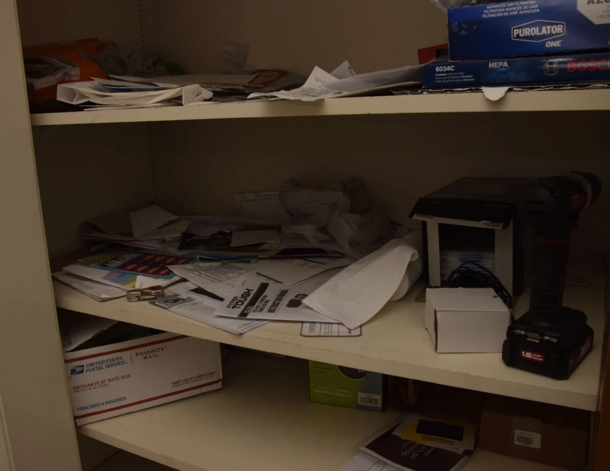 Closet shelves with loose papers, boxes and a cordless drill.