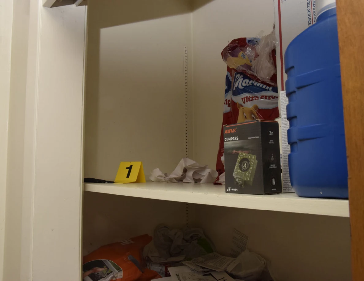 Storage shelf with a yellow marker numbered 1 beside a dark item, paper and boxed supplies.