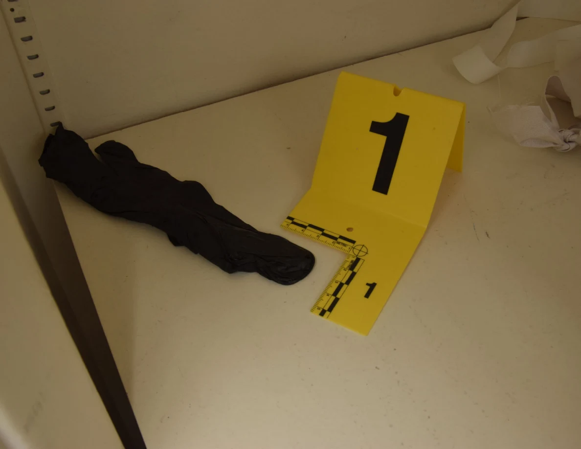 Black glove-shaped item on a shelf beside yellow marker 1 and an L-shaped measuring scale.