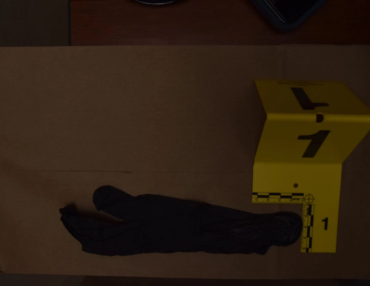 Black glove on brown paper beside a yellow numbered marker and measurement scale.