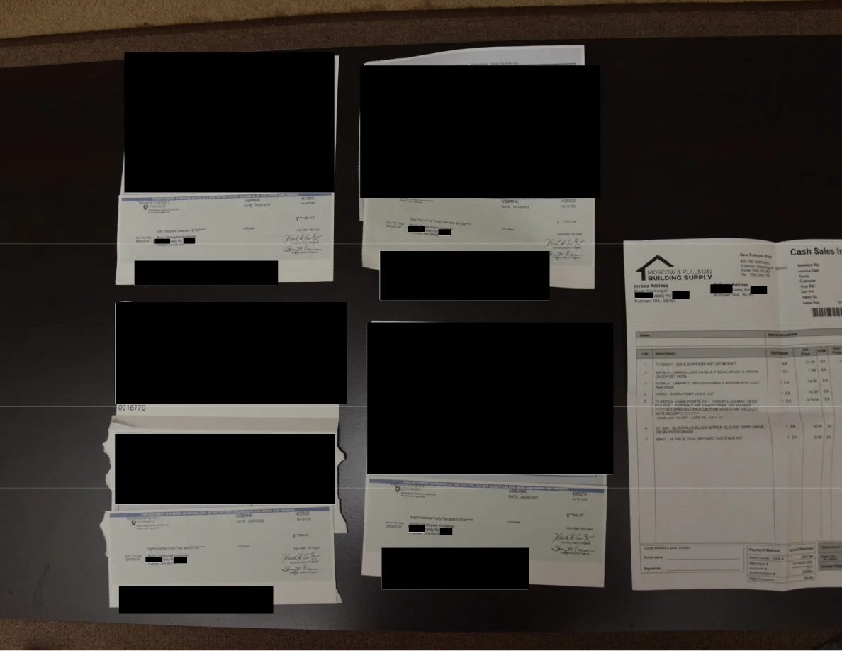 Several financial documents and an invoice on a table with large black redactions.