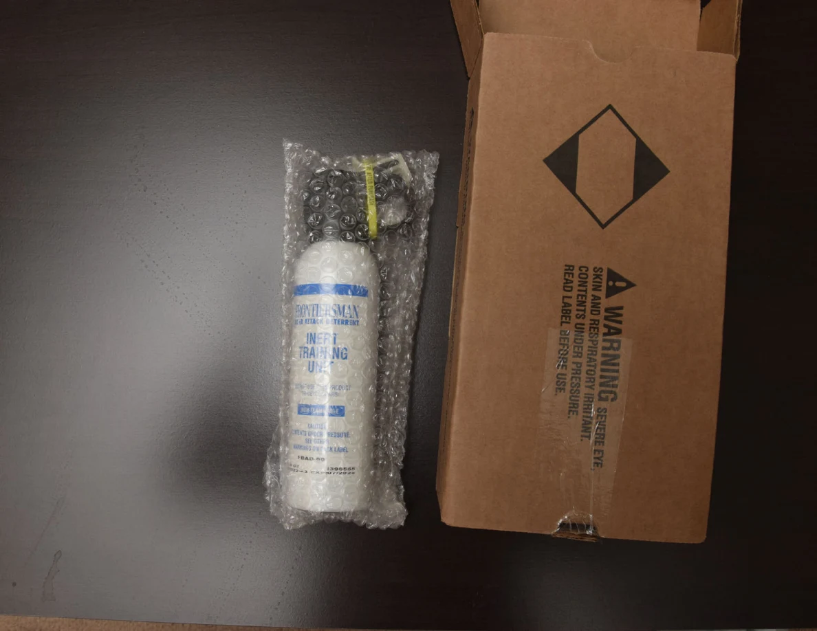 White canister wrapped in bubble wrap beside its brown warning-labeled box.