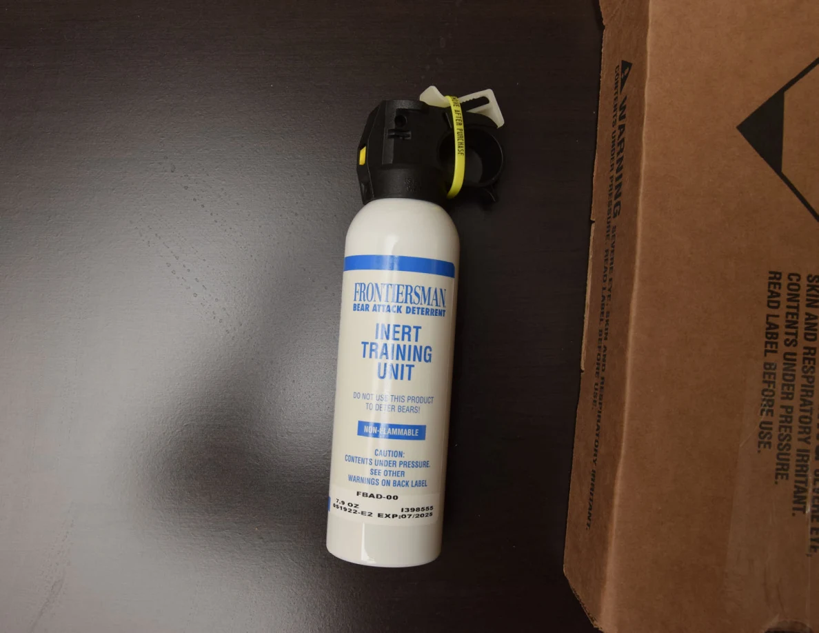 White canister labeled Inert Training Unit with black handle and yellow safety tab beside its box.