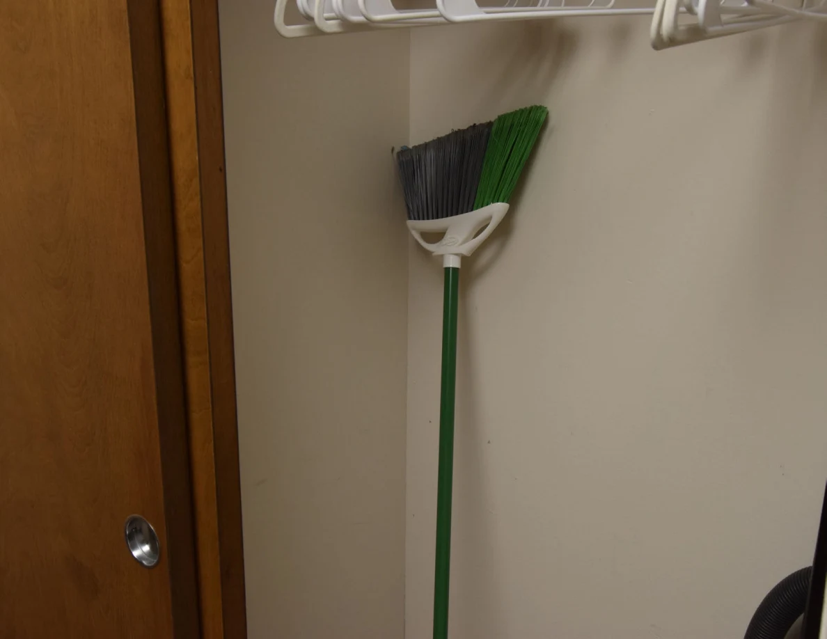 Green-handled broom stored below empty hangers in a closet.