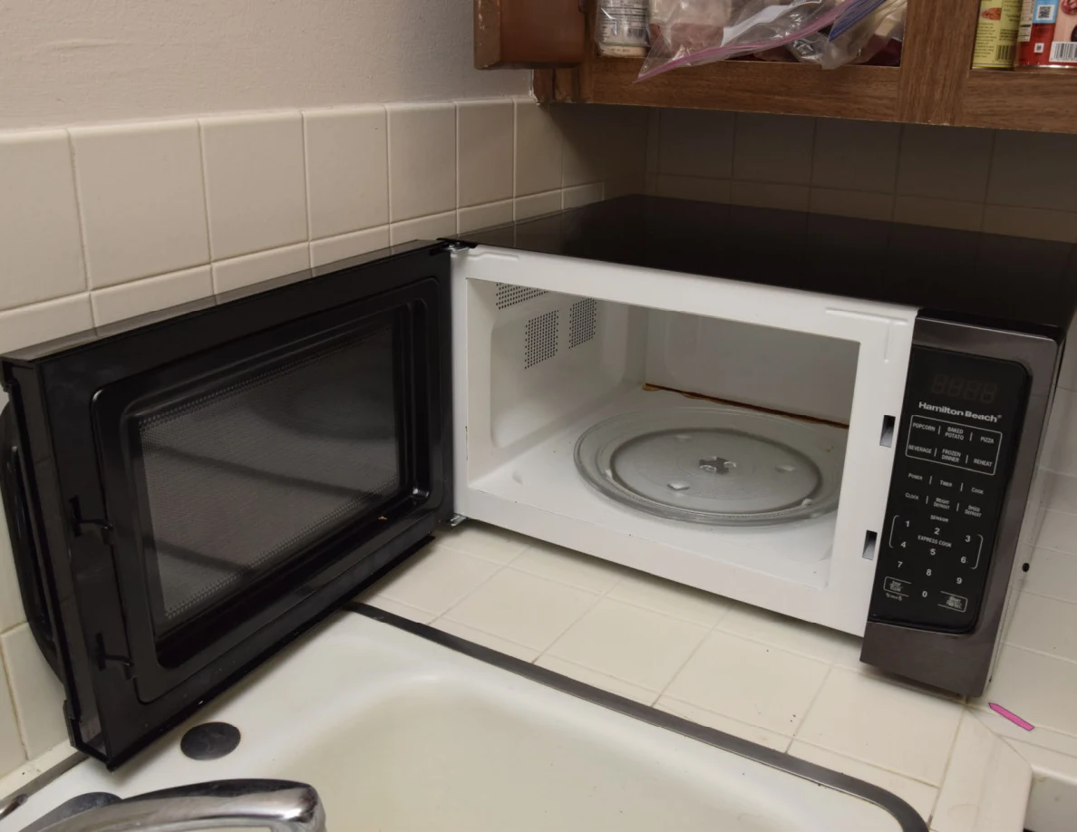 Open microwave showing its white interior and glass turntable beside a sink.