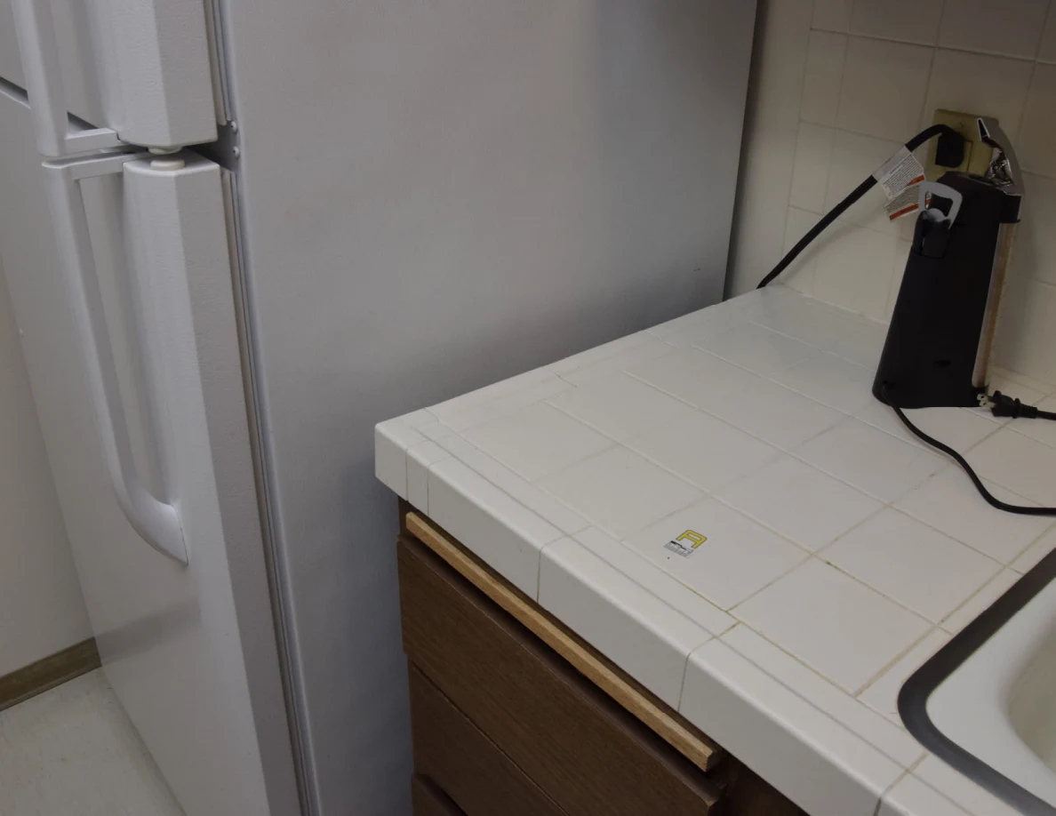 Tiled kitchen counter beside a white refrigerator and a plugged-in black device.