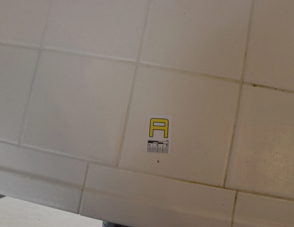 Close view of white counter tiles with a small yellow letter marker and measuring scale.