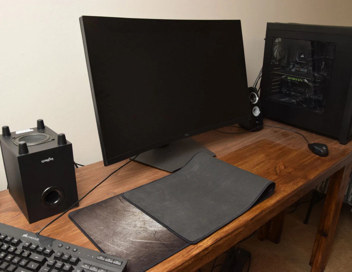 Computer desk with monitor, speakers and tower; a large desk mat is folded back.
