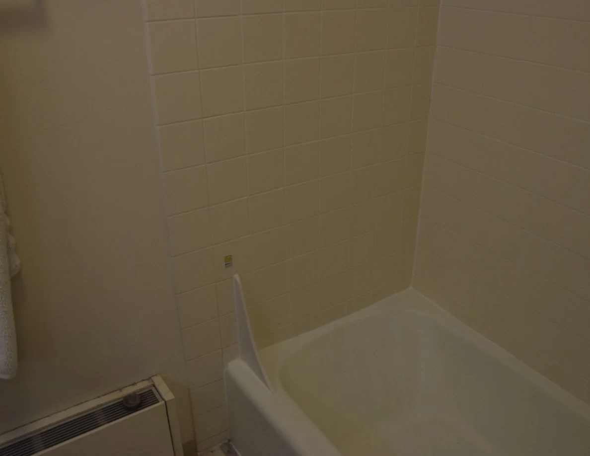 Dim bathtub corner with a small marker on the tiled wall.