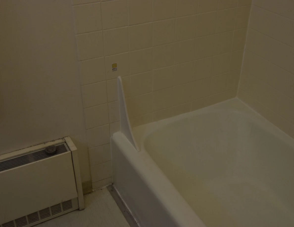 White bathtub and tiled surround with a small numbered marker near a splash guard.