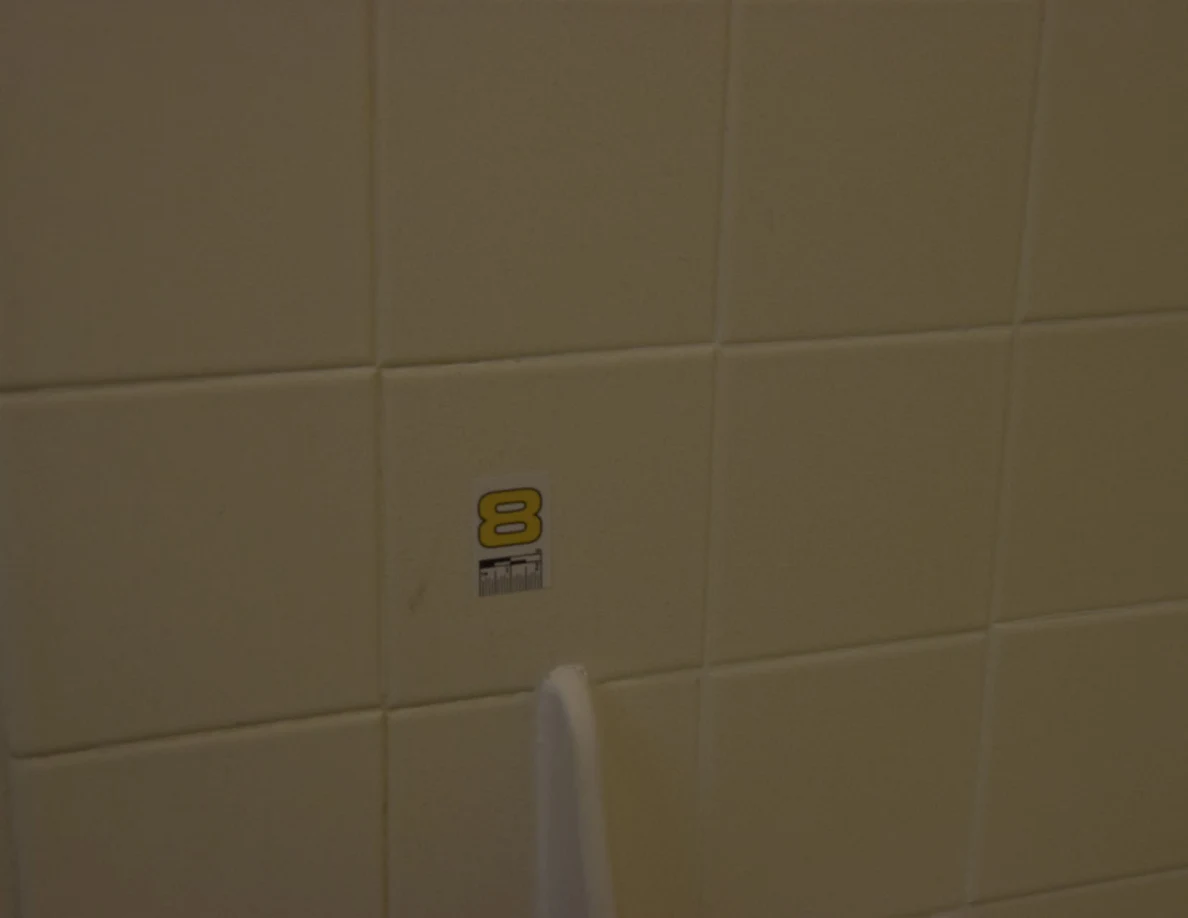 Close view of a small yellow number 8 marker on a white wall tile.