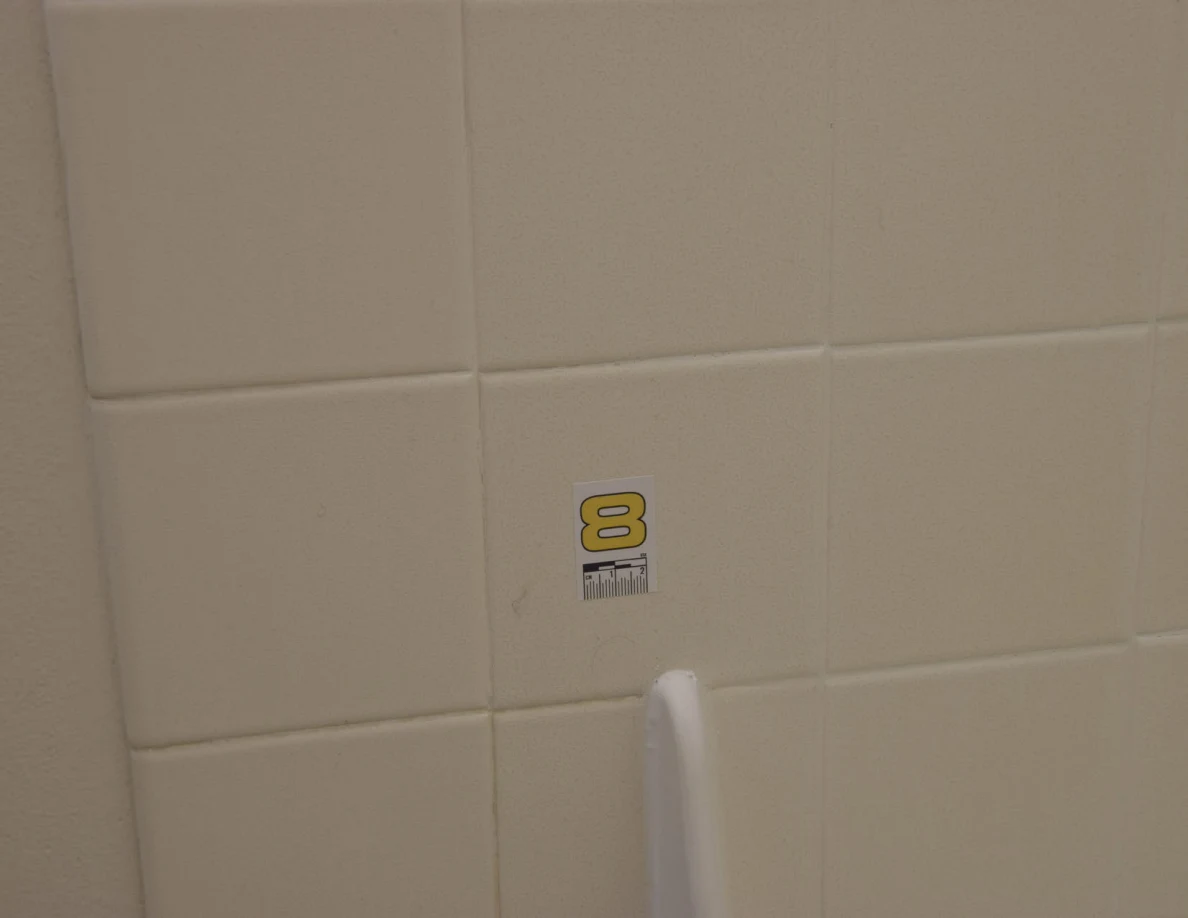 White tile with a number 8 marker above a bathtub splash guard.