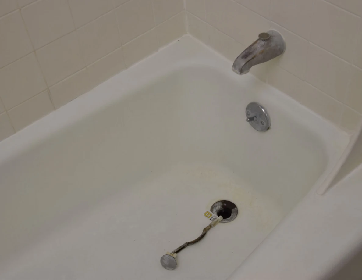 Bathtub with drain opening and detached drain linkage lying beside it.