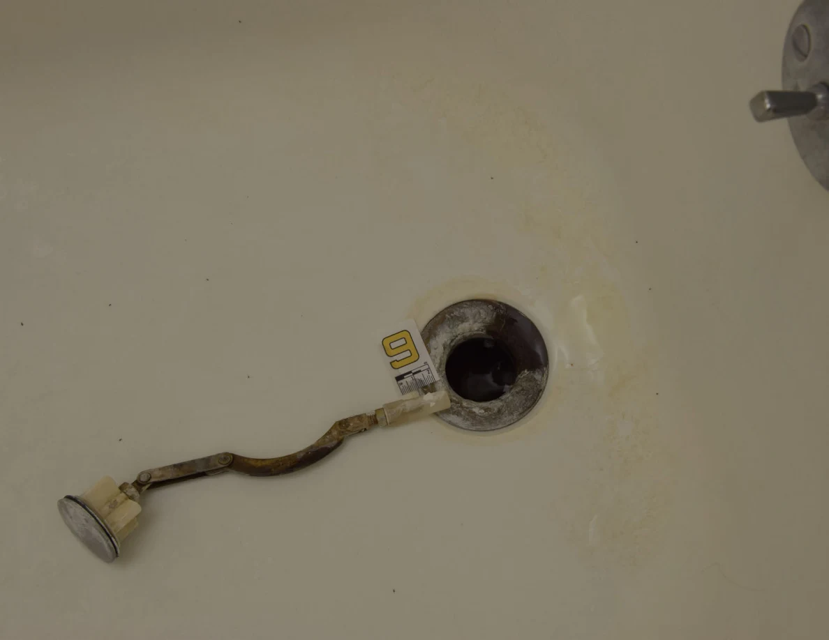 Close view of bathtub drain opening, detached linkage and number 9 marker.