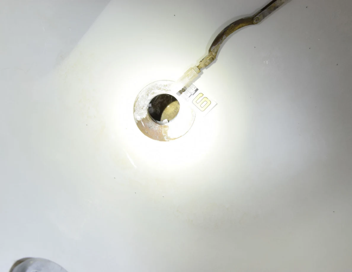 Brightly illuminated bathtub drain and detached linkage beside a small numbered marker.