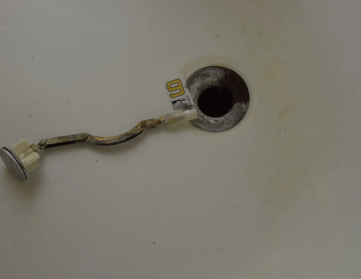Drain opening with a metal linkage laid across the bathtub floor beside marker 9.