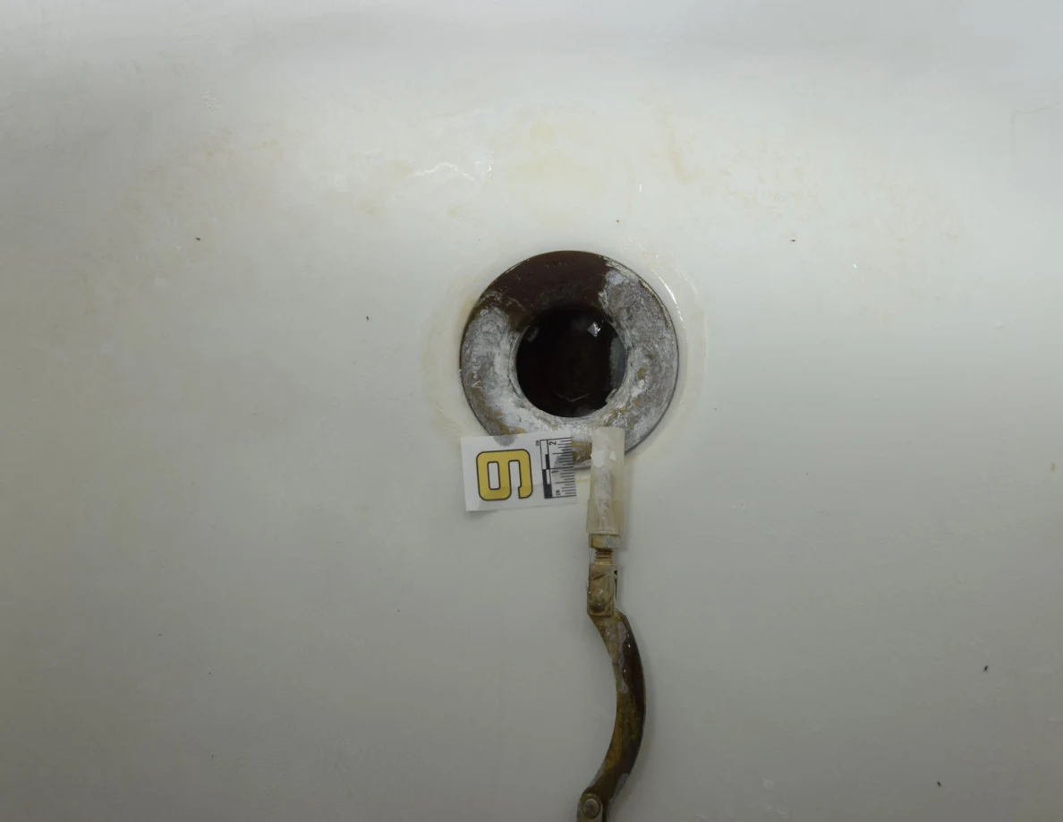 Close view of an open bathtub drain beside a small numbered marker.