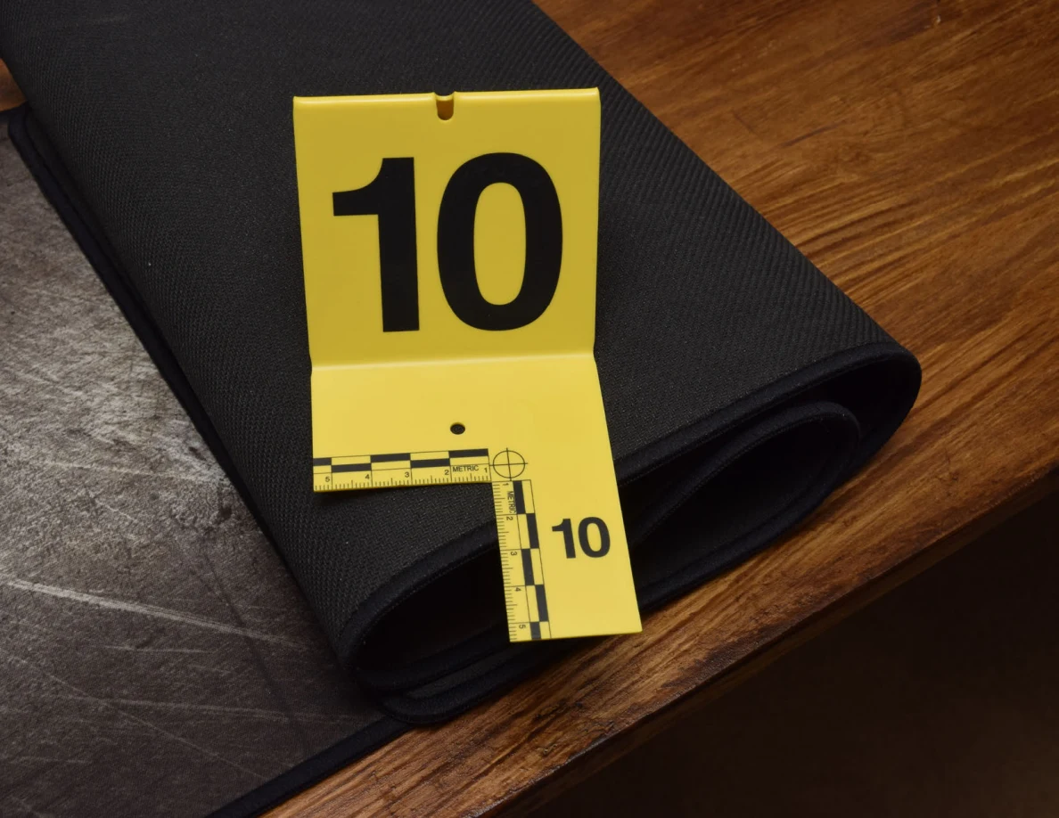 Rolled black desk mat beside yellow marker 10 on a wooden desk.