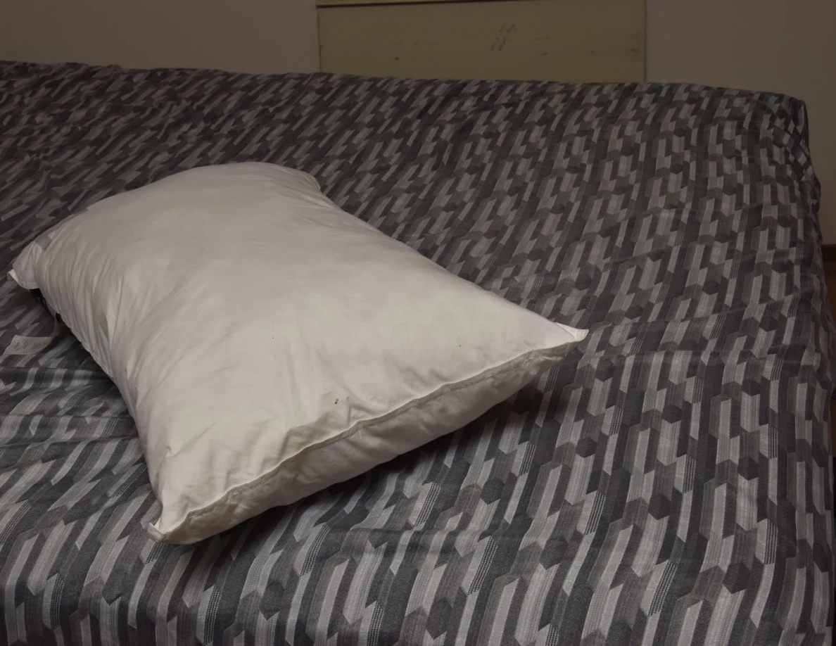 White pillow on a gray patterned bed cover, seen from the side.