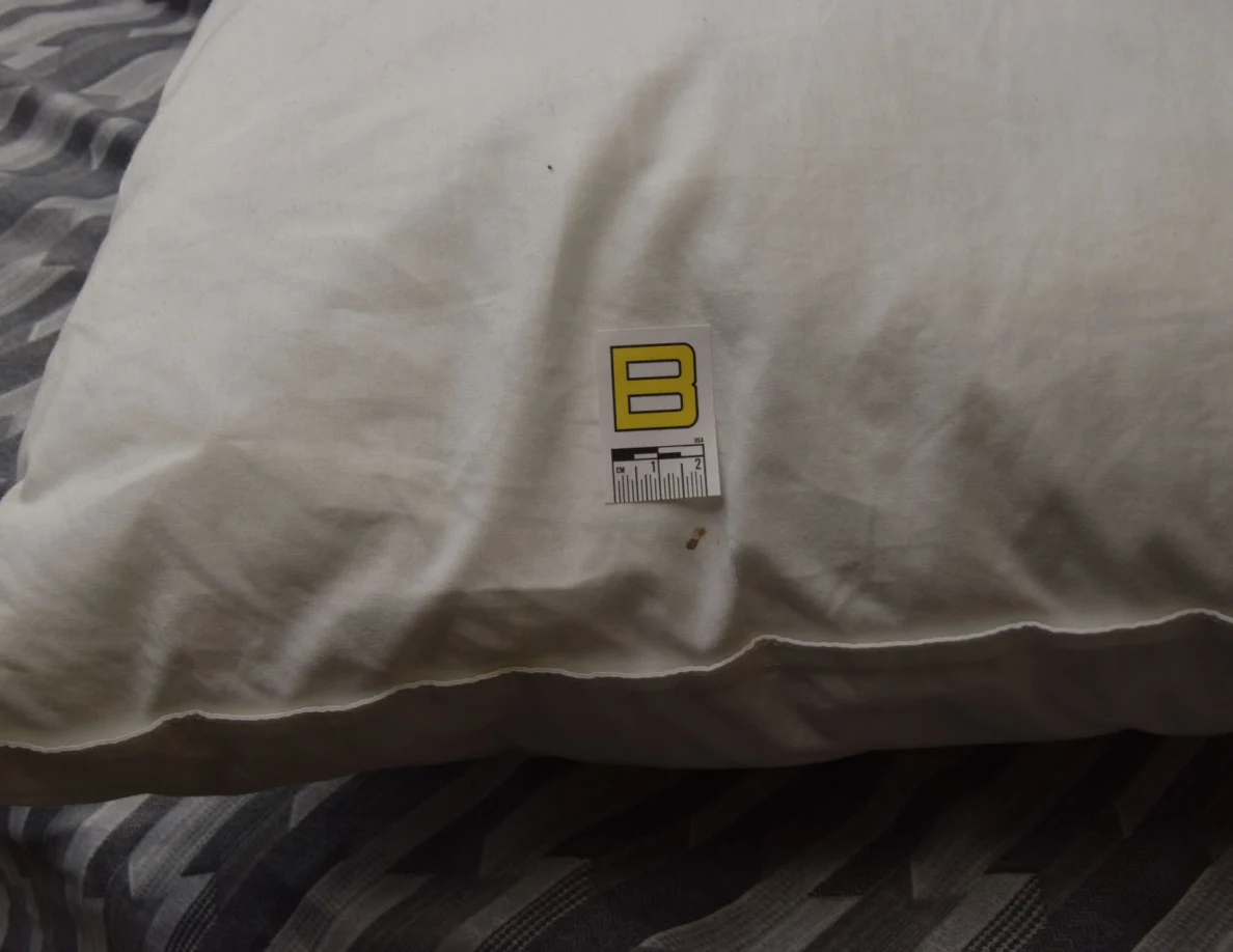 Close view of white pillow fabric and seam beside letter B marker.