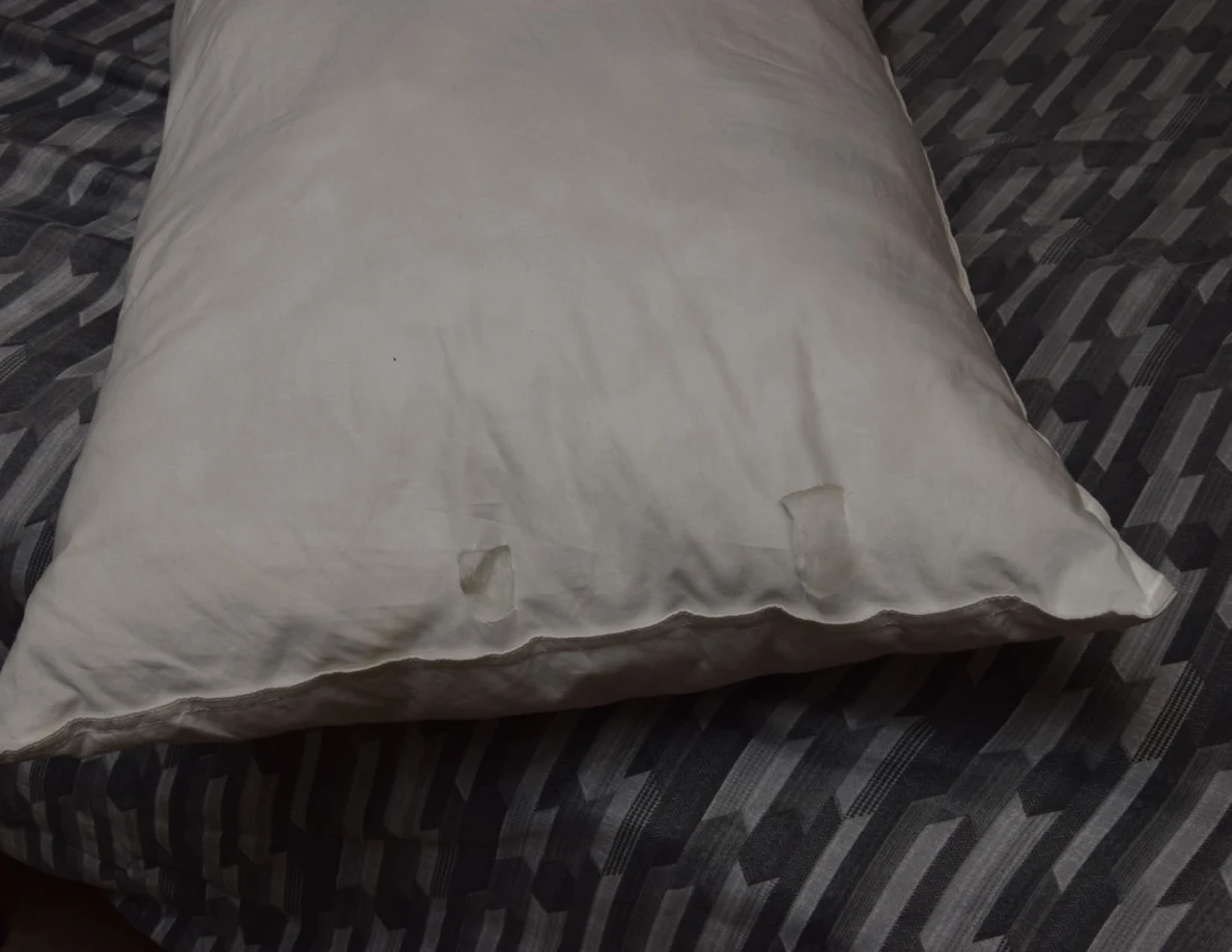 White pillow with two small rectangular areas of surface disruption near its edge.