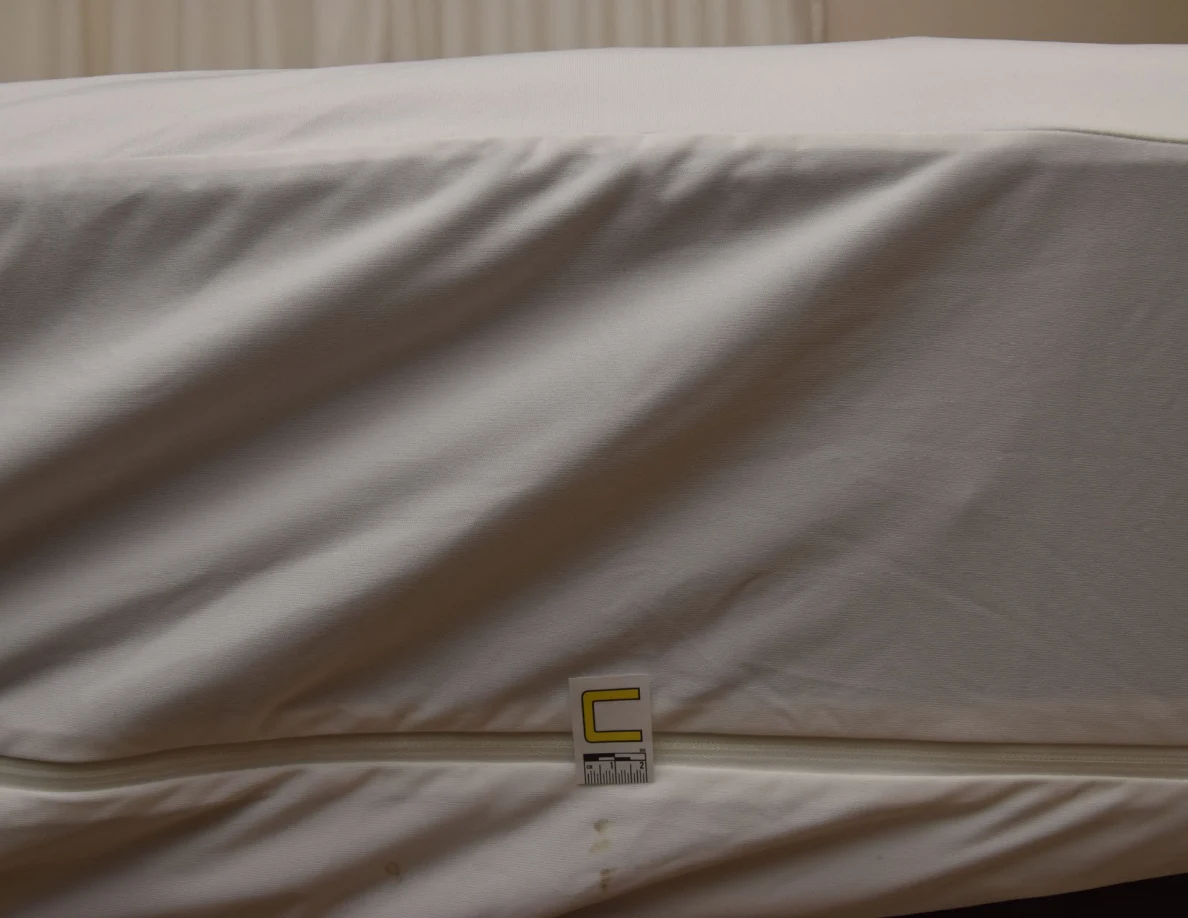 Close view of a white mattress-cover seam and letter C marker.