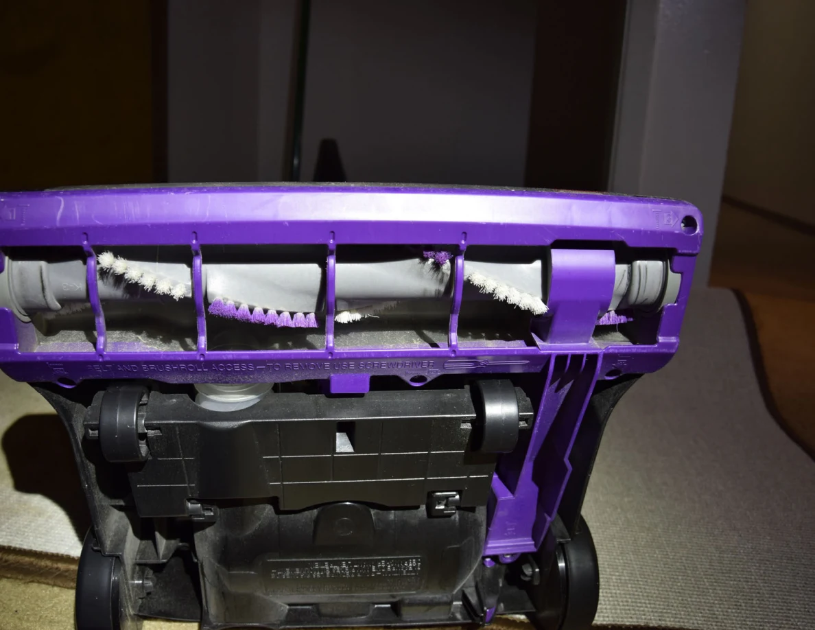 Illuminated underside of a vacuum cleaner with purple housing, wheels and brush roll.