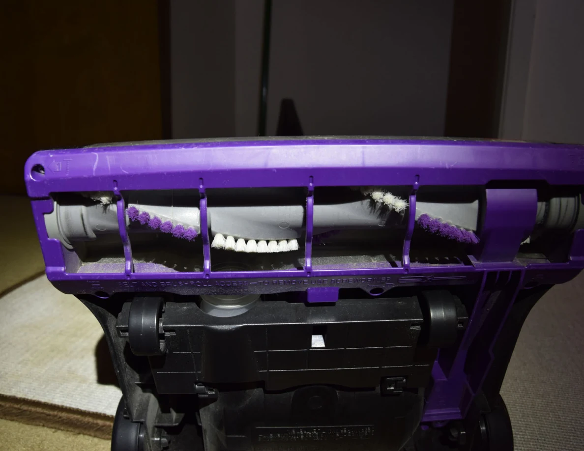 Vacuum underside with brush roll, purple housing and black wheels.