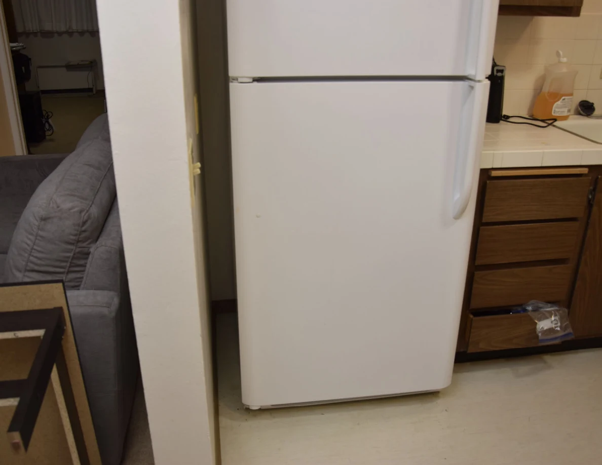 White refrigerator beside wooden kitchen drawers and a tiled counter.