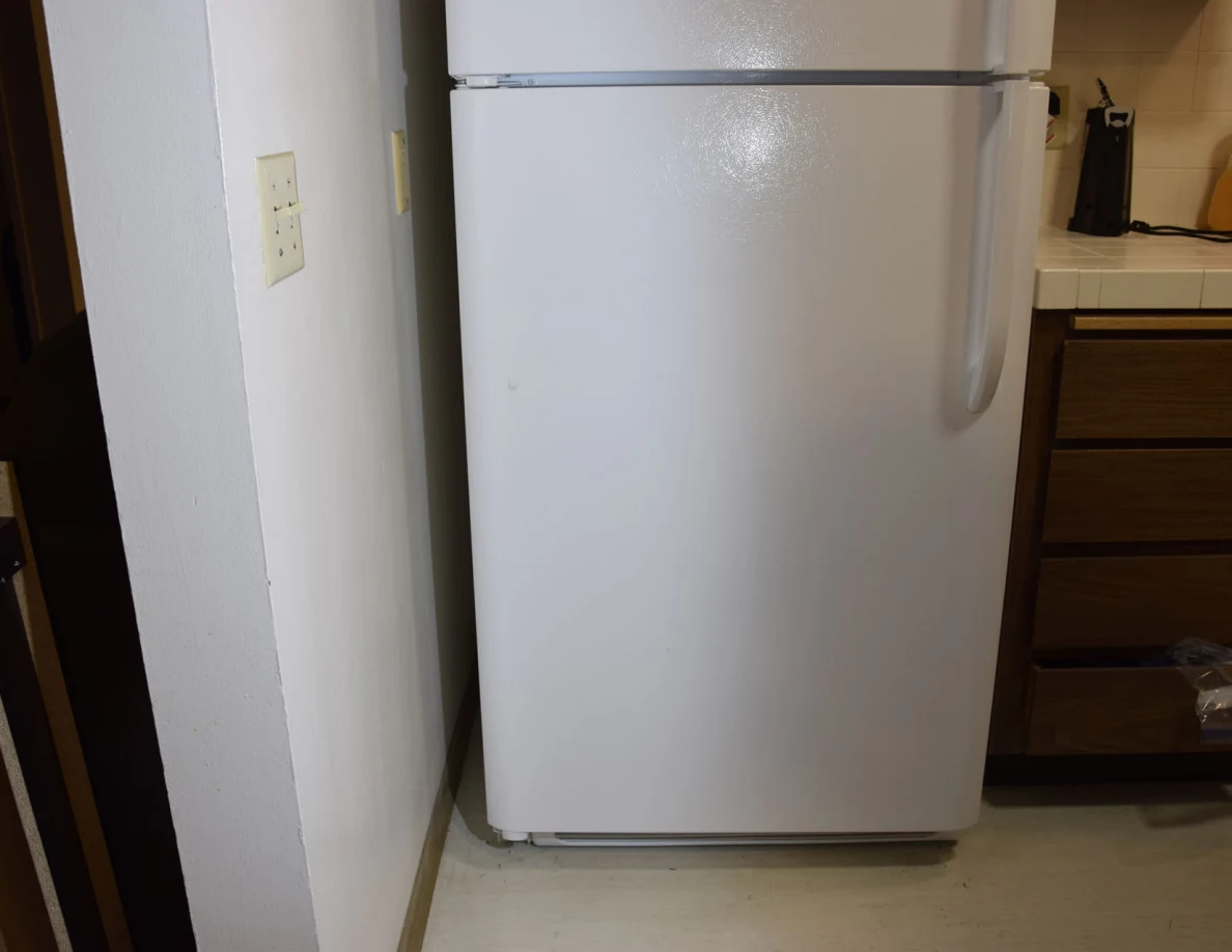 Lower refrigerator door beside a wall and wooden kitchen drawers.