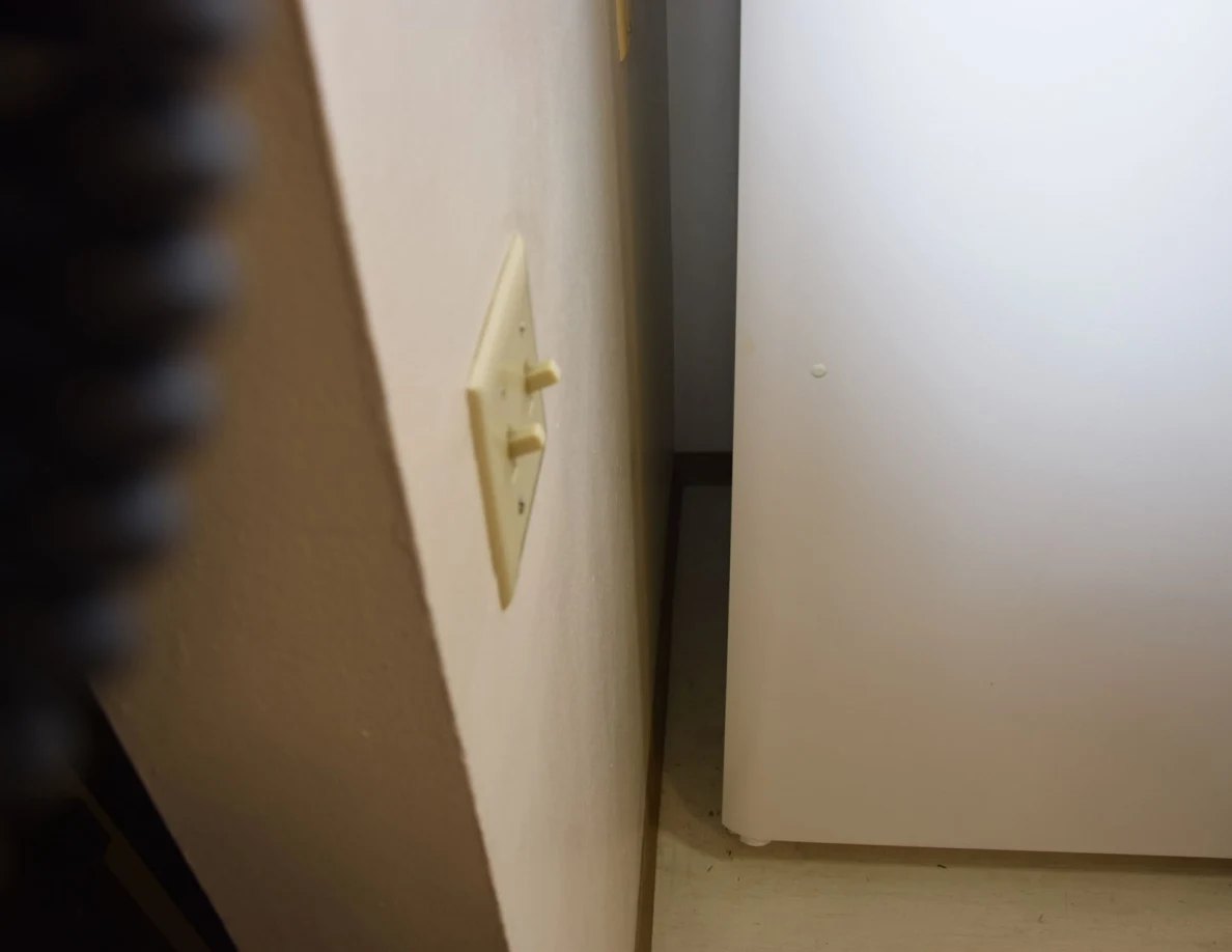 Narrow gap beside a refrigerator and wall light switches.
