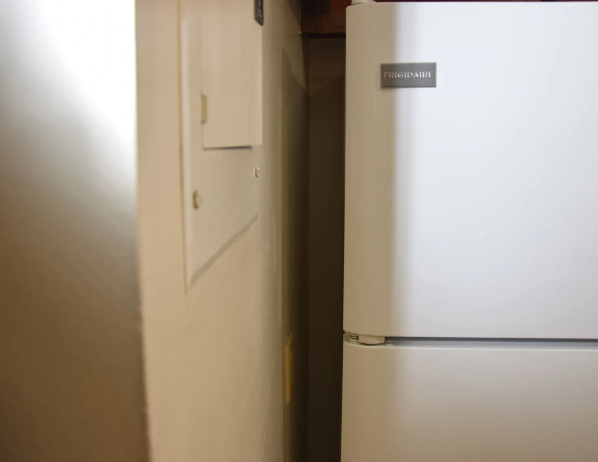 Side of a refrigerator near a small wall access panel.