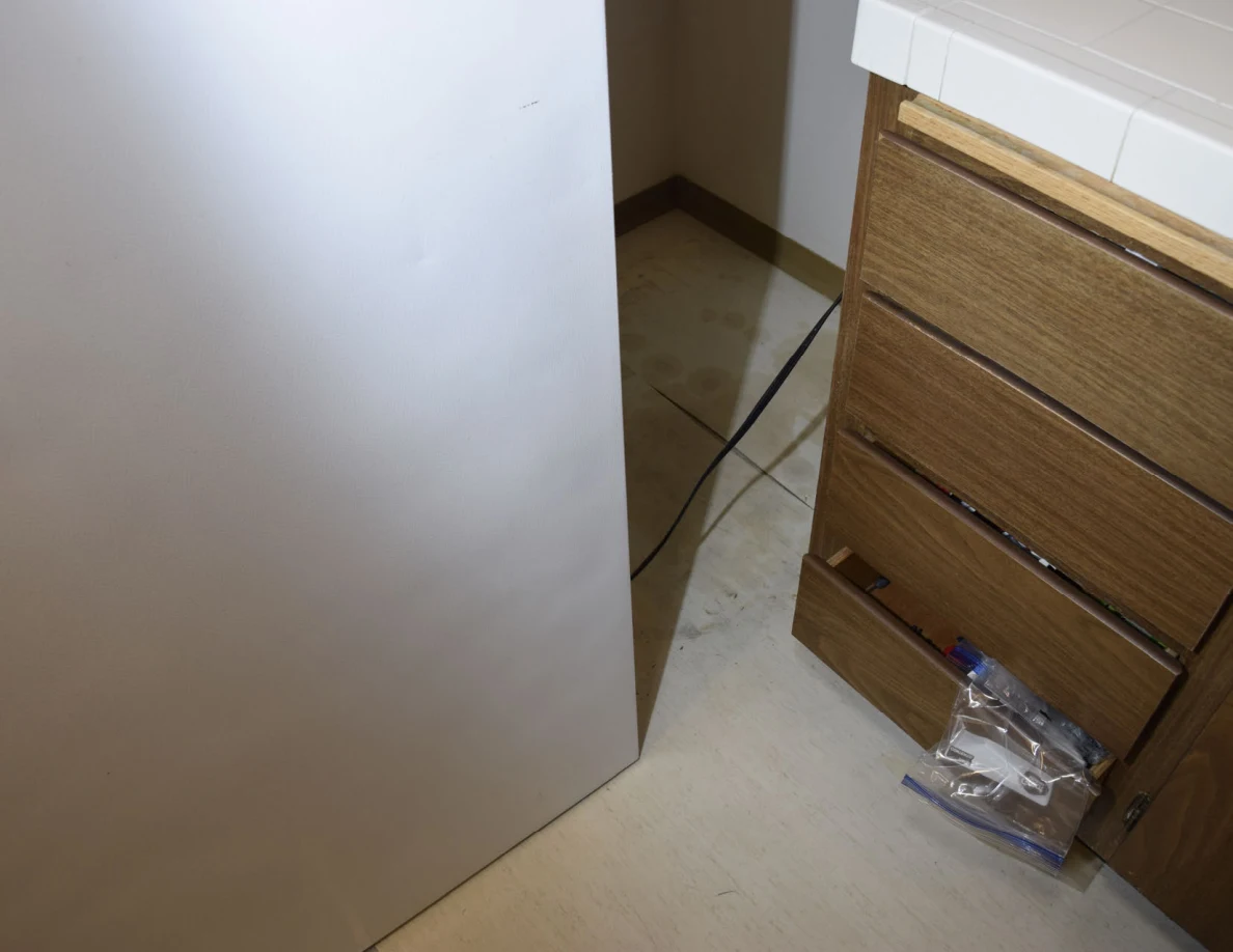 Lower refrigerator side beside wooden drawers, clear plastic bags and a trailing cord.