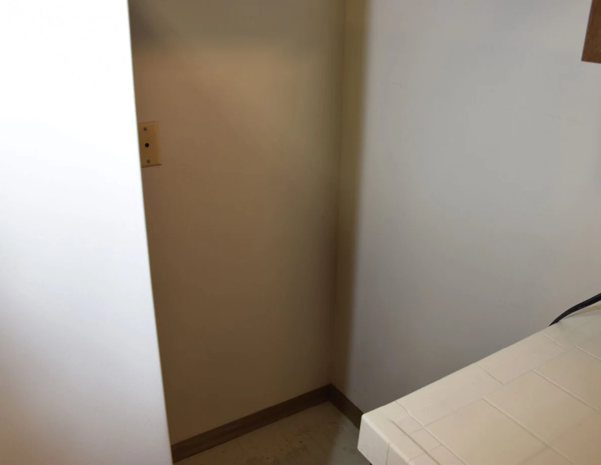 Wall corner behind a refrigerator beside a tiled counter.