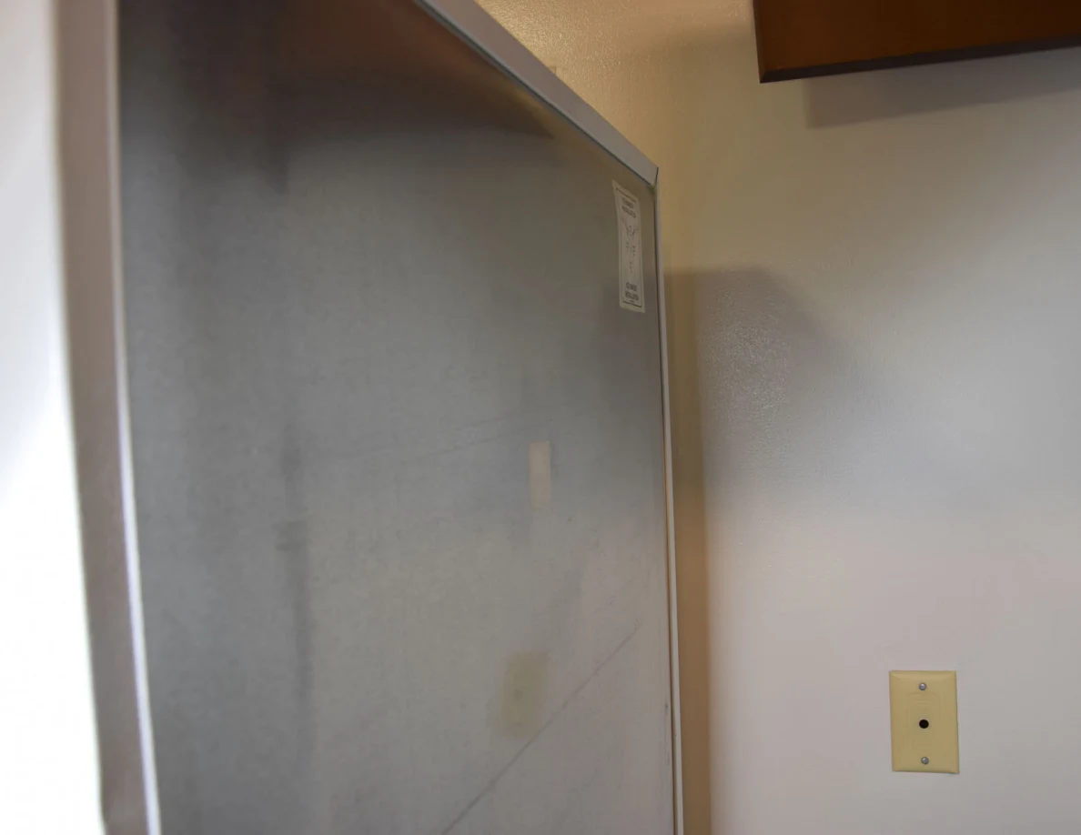 Upper metal refrigerator back beside a wall and small wall plate.