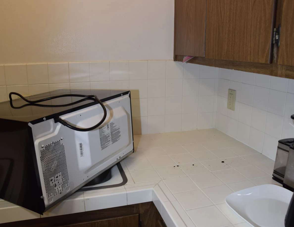 Microwave turned on its side on a tiled counter, exposing its base and cord.