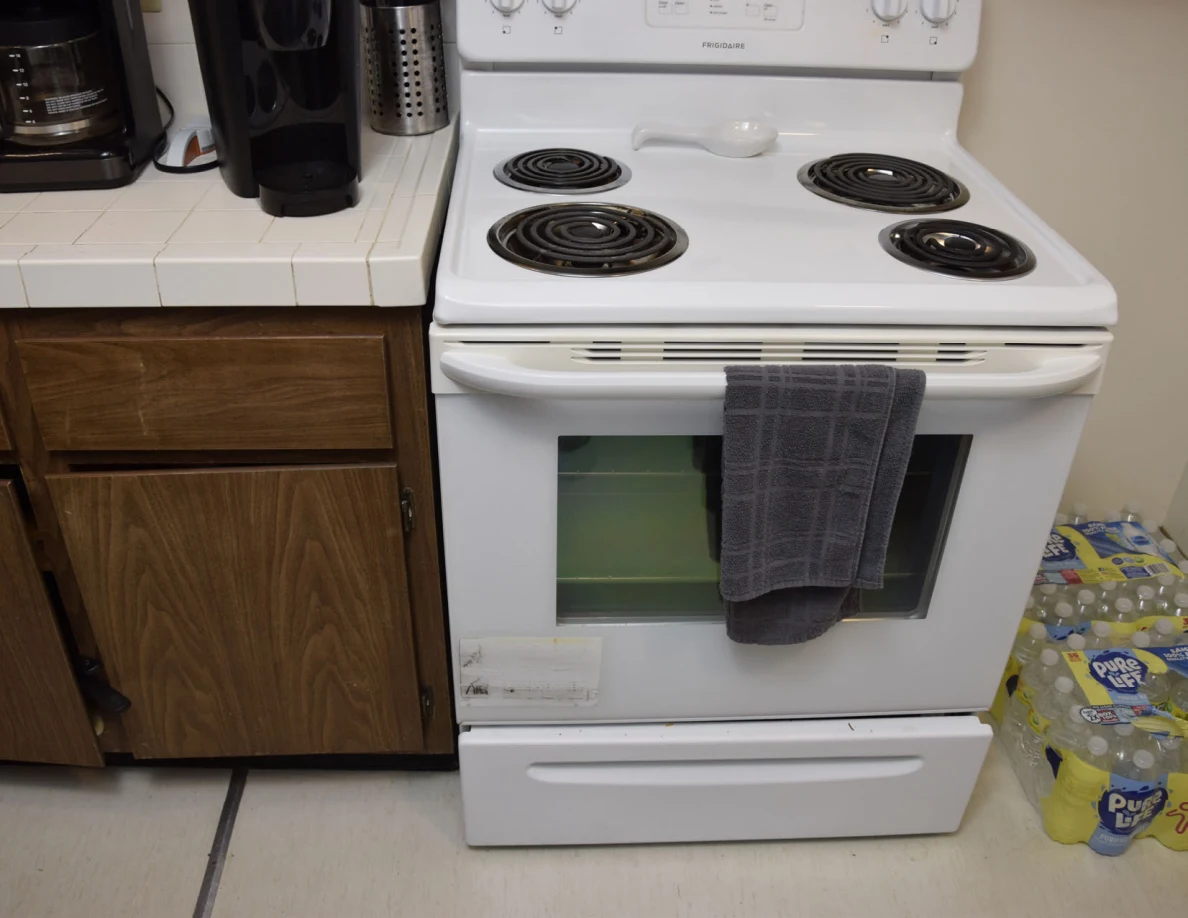 White electric stove with a gray towel on its handle and packs of drinks nearby.
