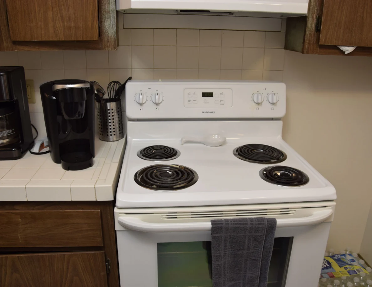 White stove beneath a range hood beside countertop appliances and utensil holder.