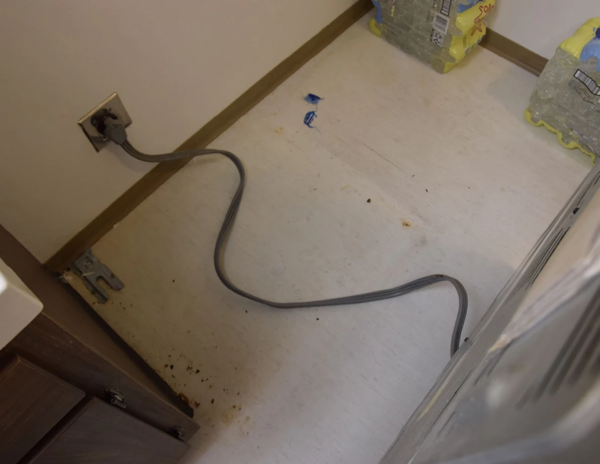 Power cord and debris on floor behind a moved kitchen range.