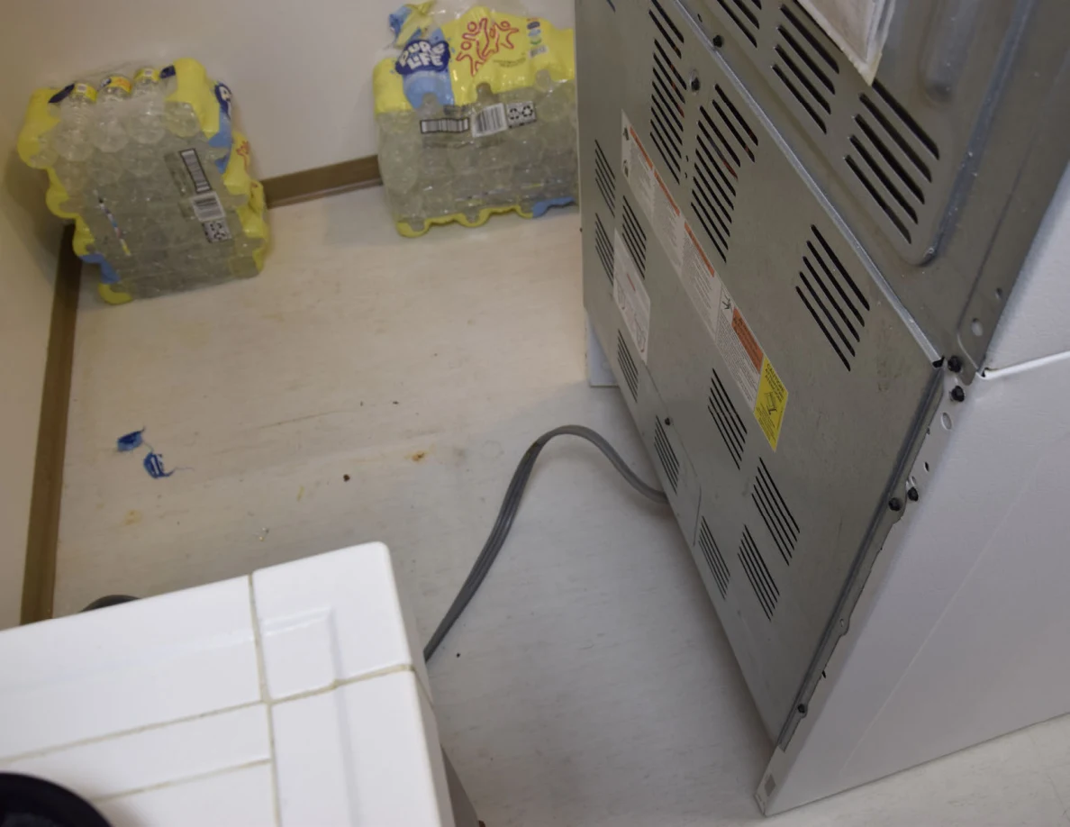 Back of a moved stove with vented metal panel and power cord across the floor.