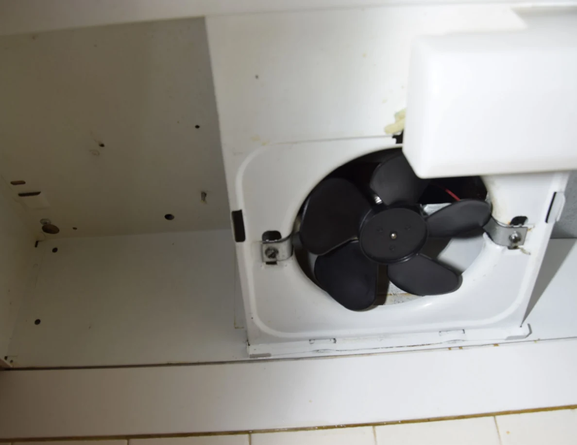 Underside of a range hood with exposed black fan blades and white housing.