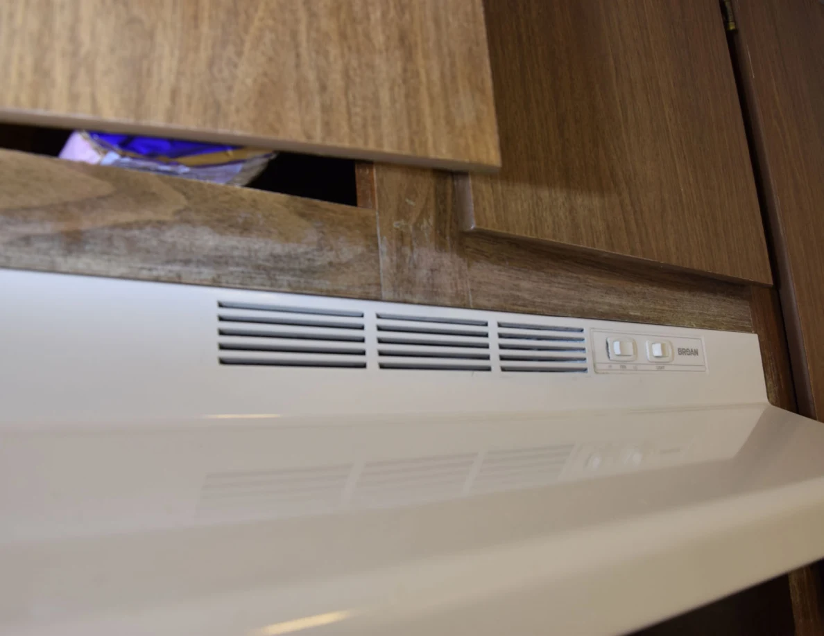 Front vents and switches of a white range hood below wooden cupboards.