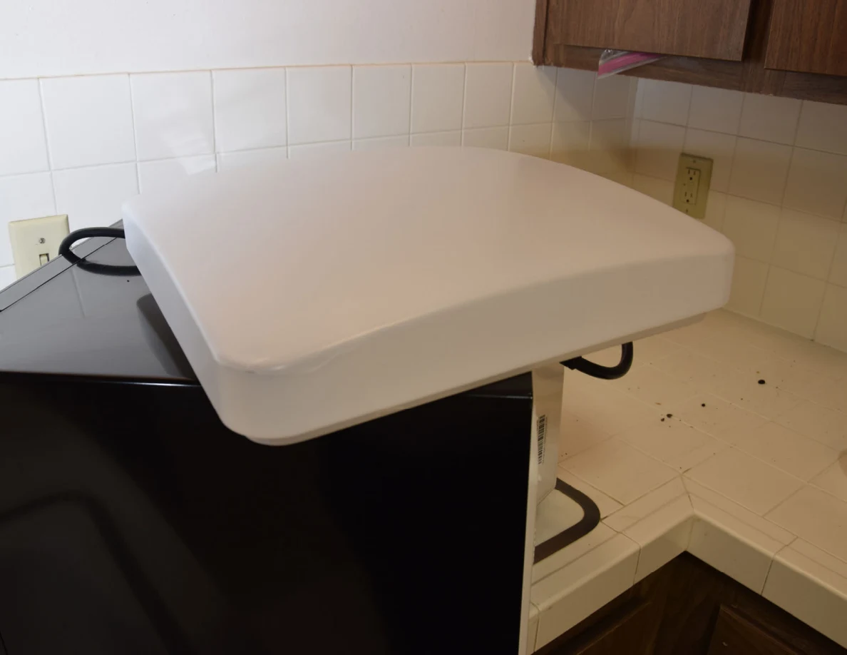 White ceiling-light cover resting on a black microwave beside a tiled counter.